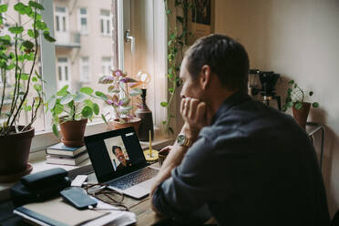 Male entrepreneur discussing with colleague on video call through laptop at home during COVID-19 - MASF23706