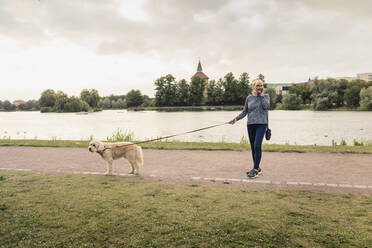 Frau mit Hund telefoniert am Seeufer mit ihrem Smartphone - MASF23771
