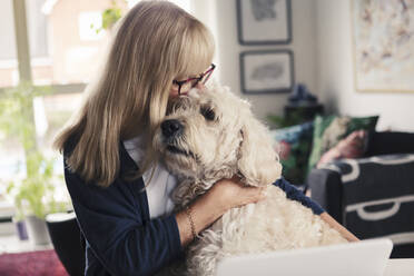 Blond woman kissing and embracing dog at home - MASF23792