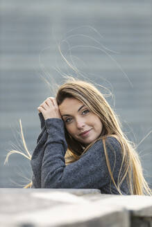 Junge Frau mit langen Haaren lehnt an einer Stützmauer - MTBF00984