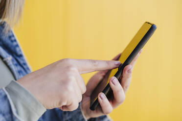 Frau benutzt Mobiltelefon an gelber Wand - EBBF03442