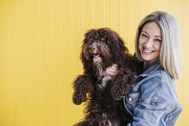 Lächelnde Frau mit Hund an gelber Wand - EBBF03444