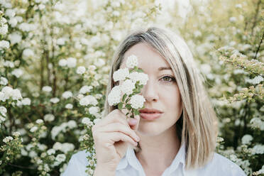 Attractive woman covering eye with bunch of flowers during springtime - EBBF03461