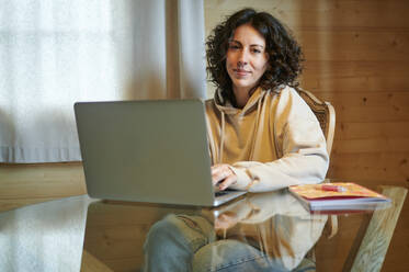 Woman with laptop sitting at table in living room - KIJF03810