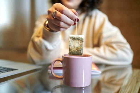 Mid adult woman holding tea bag at home - KIJF03812