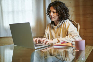Curly haired woman using laptop at home - KIJF03813