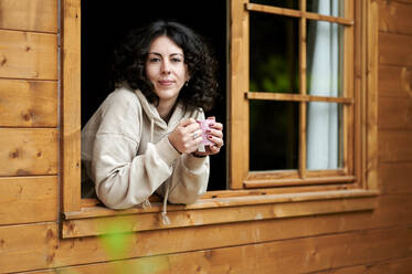 Frau mit Becher am Fenster lehnend - KIJF03827