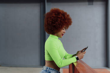 Afro woman using mobile phone at railing - PGF00550