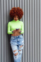 Fashionable woman using mobile phone in front of shutter - PGF00551