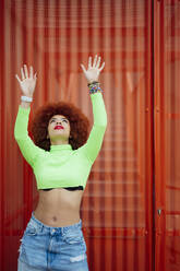 Afro-Frau mit erhobenen Armen vor einer Metallwand stehend - PGF00554