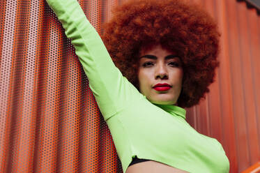 Afro hairstyle woman with hand raised in front of red metal wall - PGF00564
