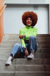 Lächelnde Frau mit Afrofrisur auf einer Treppe sitzend - PGF00566