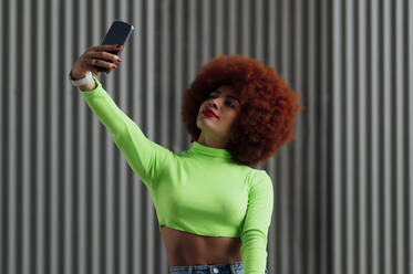 Rothaarige Frau nimmt Selfie durch Handy vor grauer Wand - PGF00572