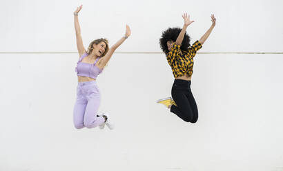 Freundinnen springen mit erhobenen Armen durch die Wand - JCCMF02345