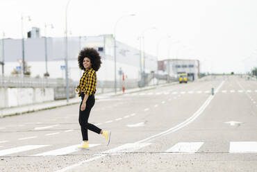 Young woman with curly hair crossing road - JCCMF02367