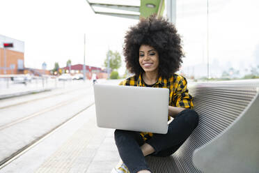 Lächelnde Frau, die einen Laptop benutzt und auf einer Bank sitzt - JCCMF02371