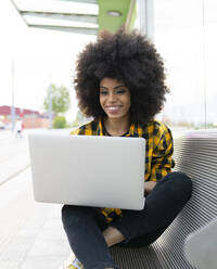 Frau benutzt Laptop, während sie auf einer Bank im Freien sitzt - JCCMF02372