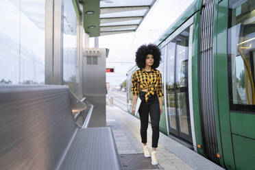 Young woman with laptop walking on platform at railroad station - JCCMF02383