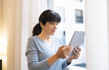 Smiling woman using digital tablet at hotel suite - JCCMF02397