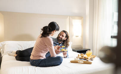 Lächelnder Mann sieht Frau beim Frühstück im Bett an - JCCMF02409