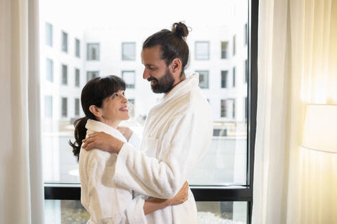 Älteres Paar in Bademänteln umarmt sich in einer Hotelsuite - JCCMF02411
