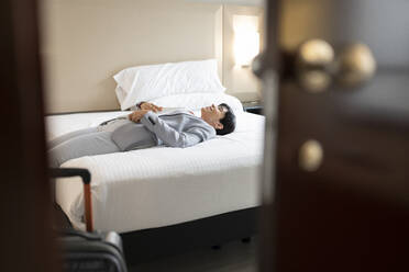 Reife Frau in Businesskleidung auf dem Bett einer Hotelsuite liegend - JCCMF02415