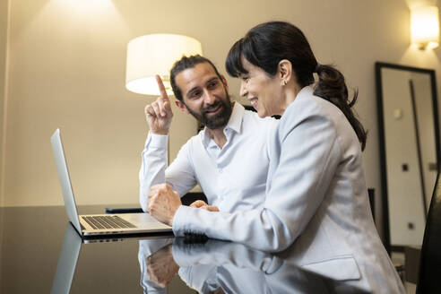 Reifes Paar in Geschäftskleidung diskutiert vor einem Laptop in einer Hotelsuite - JCCMF02417