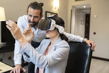 Mature businesswoman wearing virtual reality simulator by male colleague in hotel - JCCMF02418