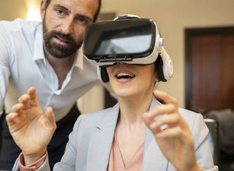 Mature businesswoman using virtual reality headset by male colleague at hotel suite - JCCMF02419