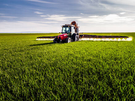 Tractor spraying pesticide on green agricultural field - NOF00185