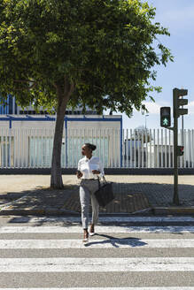 Unternehmerin beim Überqueren der Straße an einem sonnigen Tag - JRVF00575