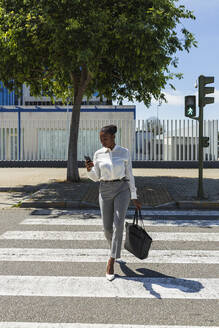 Berufstätige Frau, die ein Mobiltelefon benutzt, während sie auf der Straße geht - JRVF00576