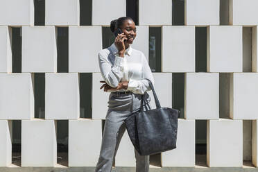 Smiling female entrepreneur talking on mobile phone in front of block shape wall - JRVF00577