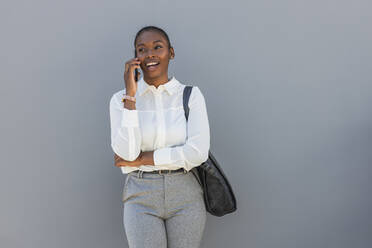 Female entrepreneur talking on mobile phone while standing in front of gray wall - JRVF00584