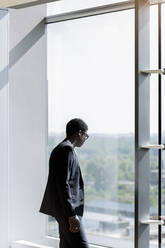 Businessman looking through window in office - BMOF00591