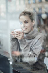 Mid adult entrepreneur with coffee cup looking through cafe window - JOSEF04381