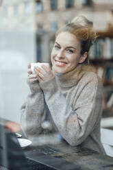 Geschäftsfrau lächelt, während sie eine Kaffeetasse am Tisch hält - JOSEF04383