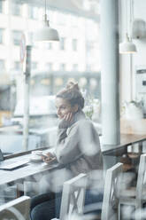 Businesswoman looking through window while sitting at coffee shop - JOSEF04386