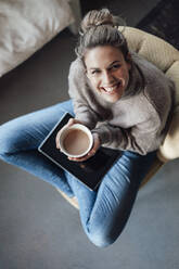 Smiling mid adult businesswoman holding drink bowl while sitting with digital tablet at cafe - JOSEF04405