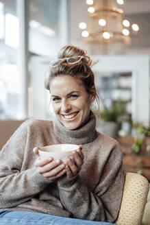 Frau lächelt, während sie eine Getränkeschale in einem Café hält - JOSEF04417