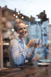 Smiling businesswoman holding coffee cup at cafe - JOSEF04422