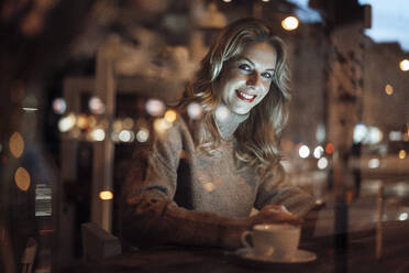 Smiling woman with digital tablet looking through cafe window - JOSEF04435