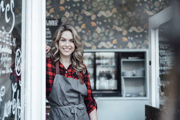 Weibliche Unternehmerin lächelt, während sie vor der Tür eines Cafés steht - JOSEF04456