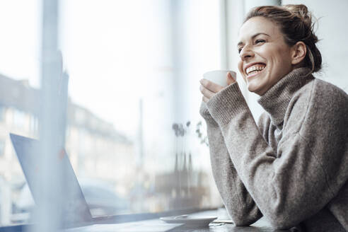 Cheerful mid adult woman holding coffee cup at cafe - JOSEF04479