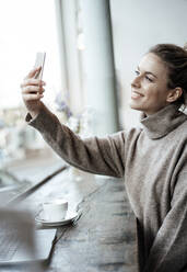 Lächelnde Kundin, die ein Selfie mit ihrem Mobiltelefon in einem Café macht - JOSEF04480