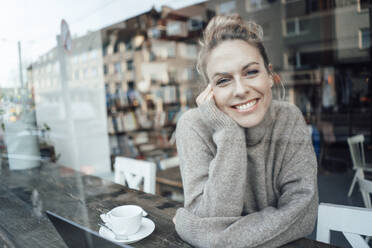 Smiling mid adult woman with hand on chin looking through cafe window - JOSEF04481