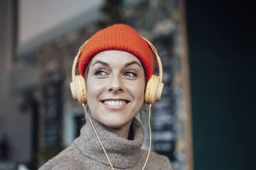 Smiling woman listening music through headphones at cafe - JOSEF04483