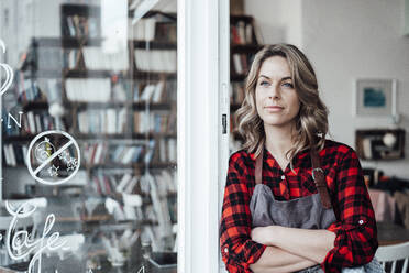 Thoughtful female waitress with arms crossed standing at cafe entrance - JOSEF04495