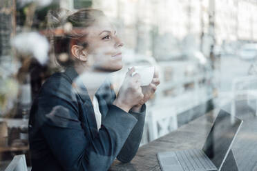 Thoughtful female entrepreneur with coffee cup looking through cafe window - JOSEF04504