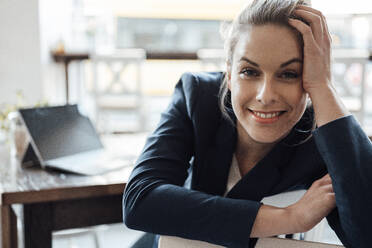 Smiling businesswoman leaning on chair at cafe - JOSEF04511